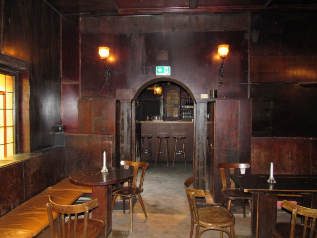 Gastraum der Bierstube Alt Berlin mit dunkler Holzvertäfelung, Bugholzstühlen und Rundbogen zum Tresen