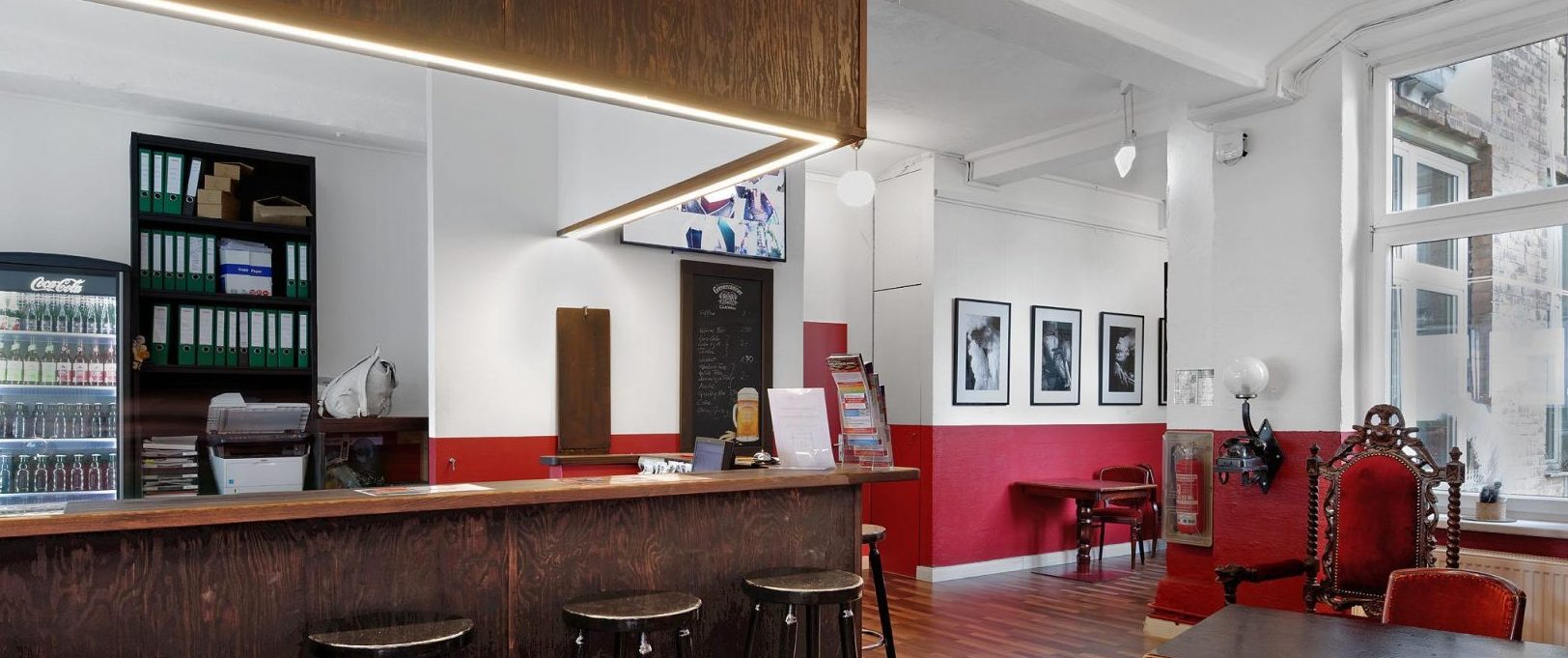Rezeption des Hostel Ballhaus Berlin mit Holztresen, Barhockern und rot-weiß gestrichener Wand